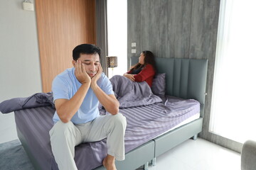 Sad frustrated middle agedasian man sit on bed after having sex while his hands touching head with upset feeling emotion and wife blurred background. Erectile dysfunction and sex problem concept