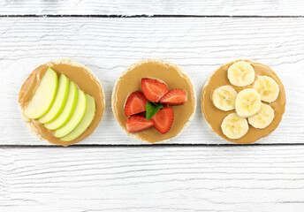 Assorted rice cakes with strawberry, banana, apple, peanut butter on white wooden background....