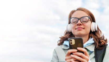Young woman with glasses listening music using her mobile phone and earphones enjoying music with closed eyes.