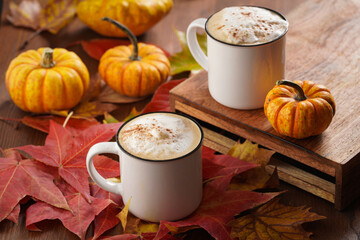 Two white cups with black coffee and white milk foam and cinnamon spice in a cozy autumn setting...