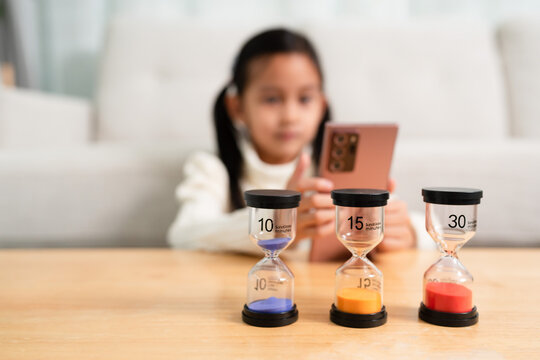 The sandclock with difference time in the background of little girl playing the smartphone. Concept of kid and technology and impact child development.