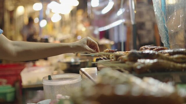 Female merchant preparing meat brochette at Chiang Mai night market - close up shot 