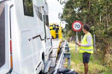 Caucasian man waiting tow truck motor home on the highway with a reflective vest and checking the vehicle