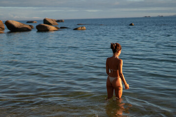 Fototapeta na wymiar Young caucasian woman entering water at sunset with white bikini