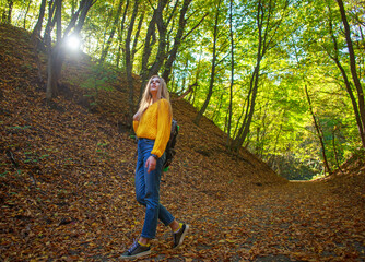 Young woman with backpack walks through the city forest park and enjoys nature on autumn sunny day
