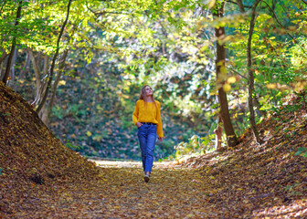 Young woman with backpack walks through the city forest park and enjoys nature on autumn sunny day