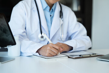 Doctor sitting at table and writing on a document report in hospital office. Medical healthcare staff and doctor service.