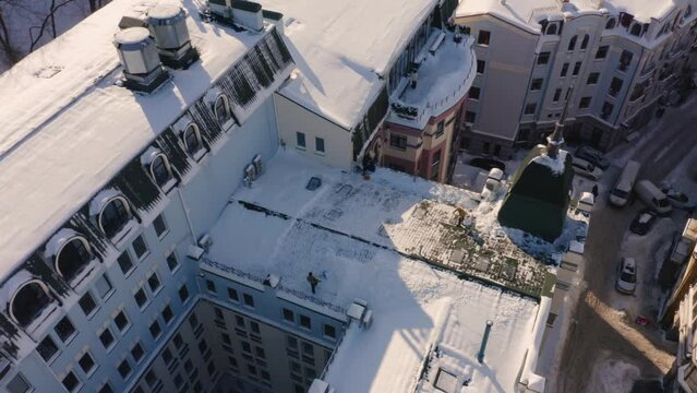 Aerial top view of sweepers cleaning roof after snowfall. European buildigs after heavy snow.