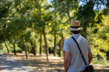 Naklejka na ściany i meble Caucasian tourist man walking in nature and staring at the landscape vertical, with a hat and a shoulder strap