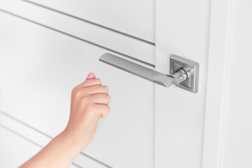 Child's hand knocking on a closed white door, inside home.