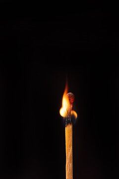 Matchstick burning in detail seen through a macro lens, black background, selective focus.