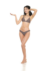 Young smiling brunette woman in bikini swimsuit advertising imaginary object on her hand on a white background.
