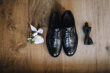 The groom's black shoes, bow tie, boutonniere lie on a wooden background.Wedding photo of accessories and details, top view.