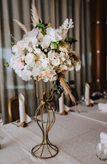 Multi-colored flowers, reeds, wild flowers stand in a metal vase, set on a table in a restaurant, as a decor. Close-up wedding photography.
