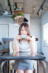 自宅でイスに座りカップを持ちながらカメラ目線で笑顔を見せる日本の若い女性