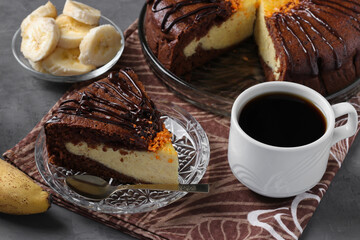 Piece homemade chocolate cake with cottage cheese and banana filling and cup of coffee on dark gray table
