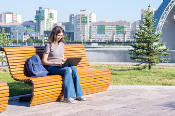Fototapeta na wymiar A Spanish student girl with glasses typing text on a laptop, looking for something on the Internet, chatting online with friends while sitting outdoors in the park. Freelance. Online learning concept