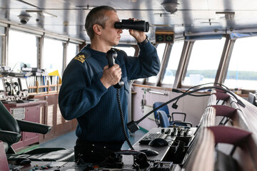 Deck officer with binoculars on navigational bridge. Seaman on board of vessel. Commercial...