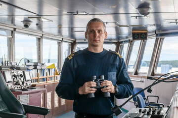 Deck officer with binoculars on navigational bridge. Seaman on board of vessel. Commercial...