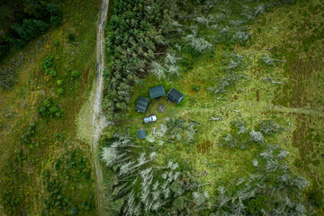 Aerial view of shelter place with huts in forest and offroad vehicle