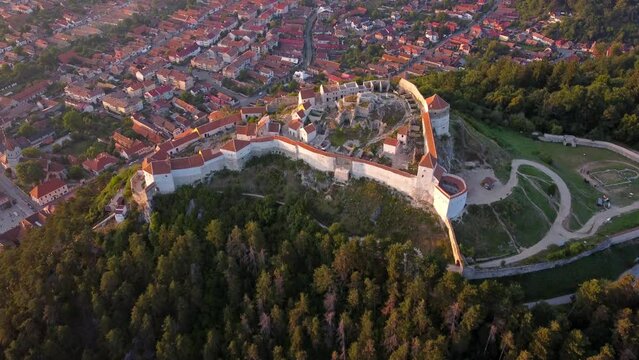 Top view of beautiful Rasnov Citadel and Rasnov town in Romania, Transylvania. Magura Codlei Peak in background. Medieval famous fortress in Brasov region. 4k drone footage near sunset.