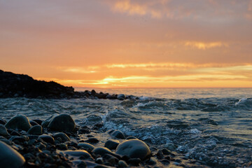Obraz premium Sunset on the rocky beach with sea waves and orange sky