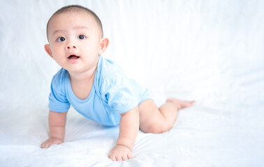 Happy family, Cute Asian newborn baby wear blue shirt lying, crawling, play on white bed with laughing smile happy face. Little innocent infant adorable child in first day of life. Mother Day concept.