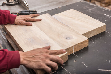 A carpenter readies 3 thick wooden boards glued together to make a large surface. A scene at a furniture workshop.