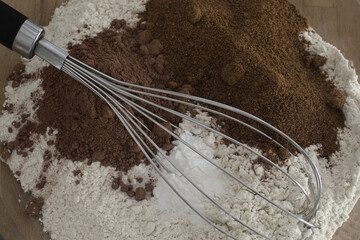 Close-up of white flour, chocolate powder, whole cane sugar and a whisk