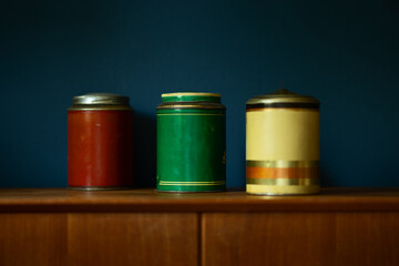 Three vintage cans on wooden table against a blue wall.