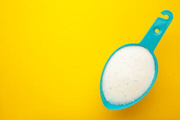 Laundry detergent powder for washing machine in plastic scoop on yellow background.