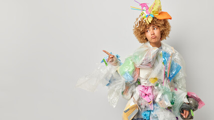 Horizontal shot of displeased curly haired female volunteer covered with plastic garbage points...
