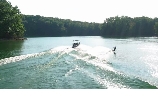 Aerial view of a wakeboarder being towed behind a ski boat on a green lake