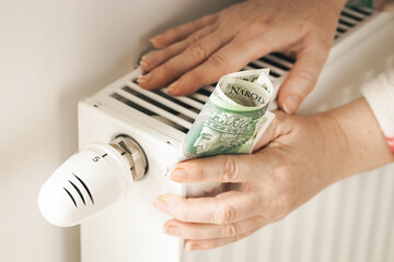 Costs of heating houses and apartments in Poland, Rising energy prices A woman touches a radiator holding a pile of 100 zlotys in her hand, Fear of winter and cold, power outages