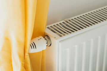 white radiator next to the yellow curtain, House and apartment heating costs, Rising energy prices,...