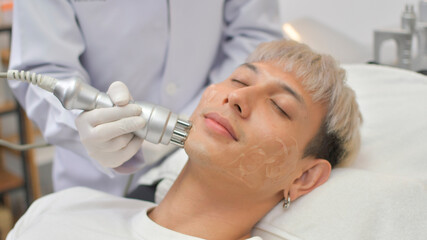 Obraz na płótnie Canvas A handsome Asian man undergoes facial rejuvenation in a beauty clinic using modern medical equipment. By certified beauty experts according to standards.