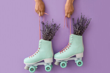 Woman holding vintage roller skates with lavender flowers on color background
