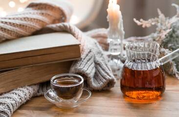 Still-life. Old books, hot tea in a glass turk, a blanket and burning candles on a wooden table in a cozy living room. The concept of a tea ceremony. Home relaxation.
