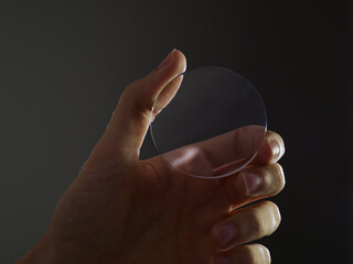 Glass lens for eyewear, hand holds a circular lens for eyewear manufacturing