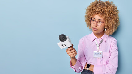 Horizontal shot of serious female journalist records daily tv news holds microphone dressed in...