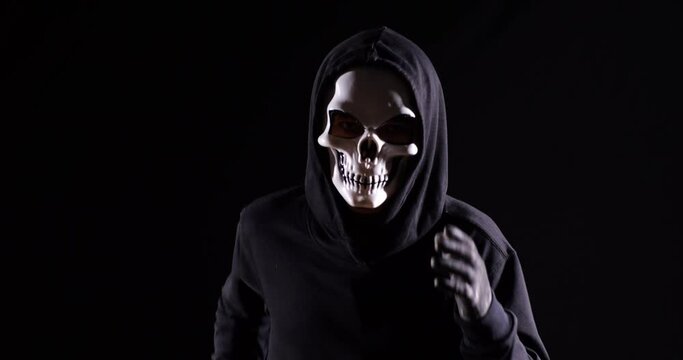 Close Up Of Scary Man In The Hooded Sweatshirt Wearing Halloween Mask Holding A Knife And Running On The Black Background 
