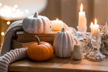 Still-life. Pumpkins, old books, a blanket and burning pumpkin-shaped candles on a wooden table in a cozy living room. Home autumn concept.