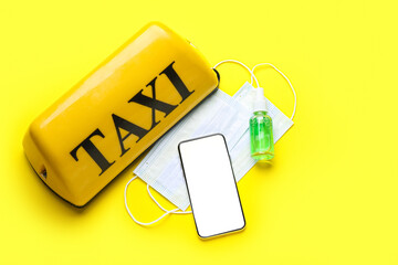 Taxi roof sign, smartphone, medical masks and sanitizer on yellow background