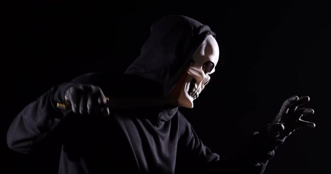 Close Up Side View Of Scary Man In The Hooded Sweatshirt Wearing Halloween Mask Holding A Knife And Making Frightening Gesture While Running On The Black Background
