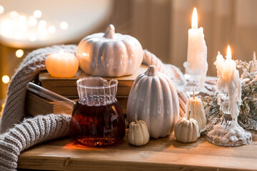 Still-life. Pumpkins, old books, hot tea, a blanket and burning pumpkin-shaped candles on a wooden table in a cozy living room. Home autumn concept.