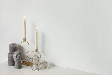 Holder with burning candles and stylish decor on chest of drawers near white wall