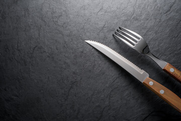 Black stone slate board with fork and knife, top view.
