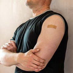 Konzeptfoto für Impfkampagne: durch ein Pflaster geschützte Impfstelle am Oberarm eines Mannes.