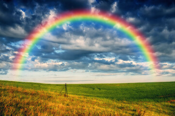 Scenic view of rainbow over green field. dramatic gray sky over a picturesque hilly field