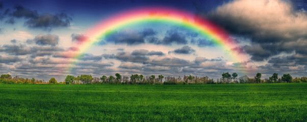 Scenic view of rainbow over green field. dramatic gray sky over a picturesque hilly field